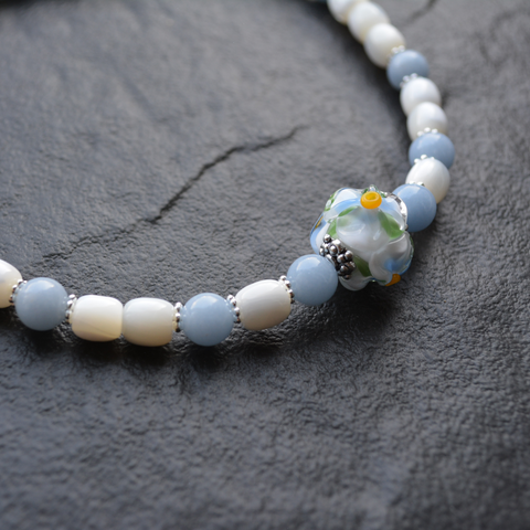 A necklace featuring mother-of-pearl, angelite, and a glass flower crafted using the lampwork technique.