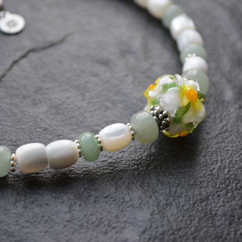 A necklace featuring mother-of-pearl, jade, and a glass flower crafted using the lampwork technique.