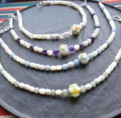 A necklace featuring mother-of-pearl, natural gemstones, and a glass flower crafted using the lampwork technique.